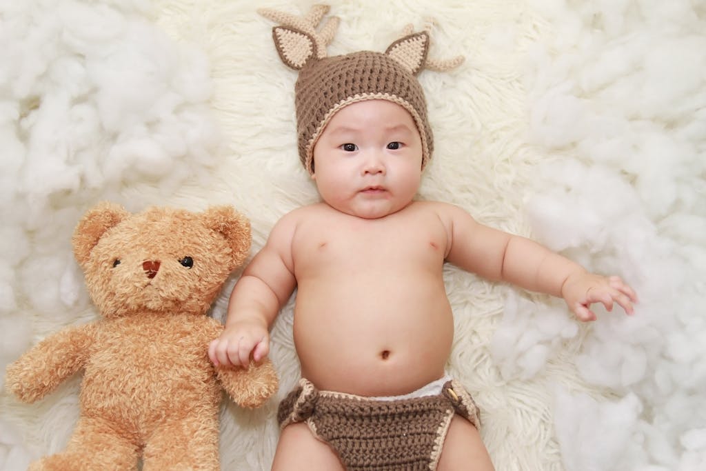 Cute baby posing with a teddy bear in a knitted outfit, exuding charm and innocence. Pediatric circumcision in calabasas