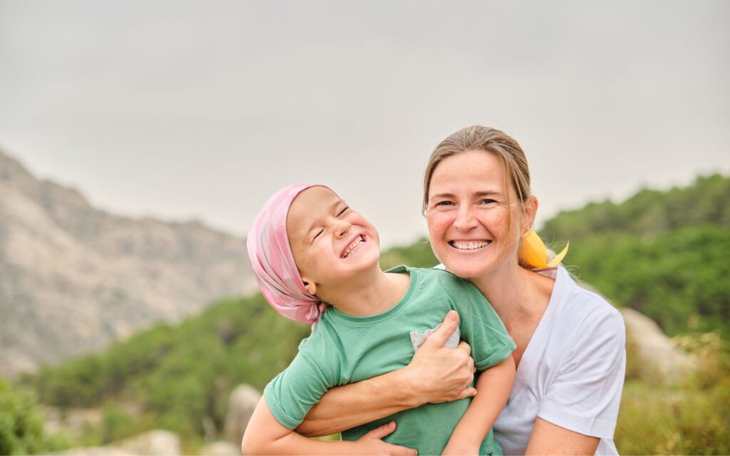 childhood tumors | Child with pediatric tumors, and mother smiling outdoors together